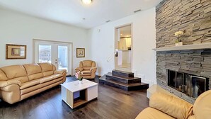 A living room with a leather sofa, a coffee table, a fireplace, and a staircase leading to an upper level. - WhiteIris-5-Bedroom Home with Pool, Mini Golf, & Heated Jacuzzi in Boynton Beach (Boynton Beach)