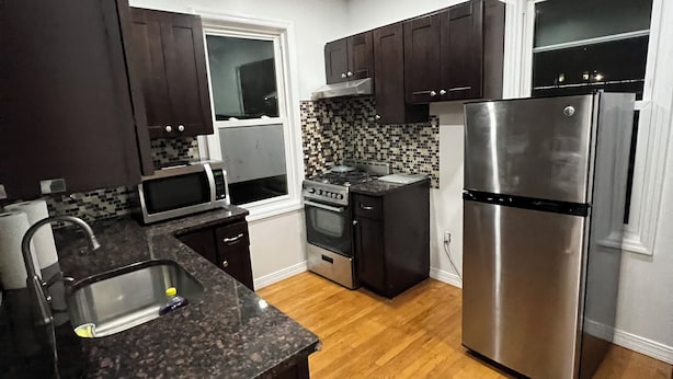 A modern kitchen with dark wooden cabinets, stainless steel appliances, a granite countertop, and a tiled backsplash.