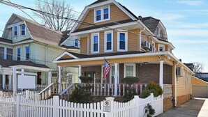 A two-story house with a front porch, a flag, and a white picket fence.