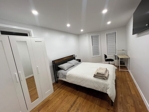 A bedroom with a bed, wardrobe, bedside table, and a TV mounted on the wall.