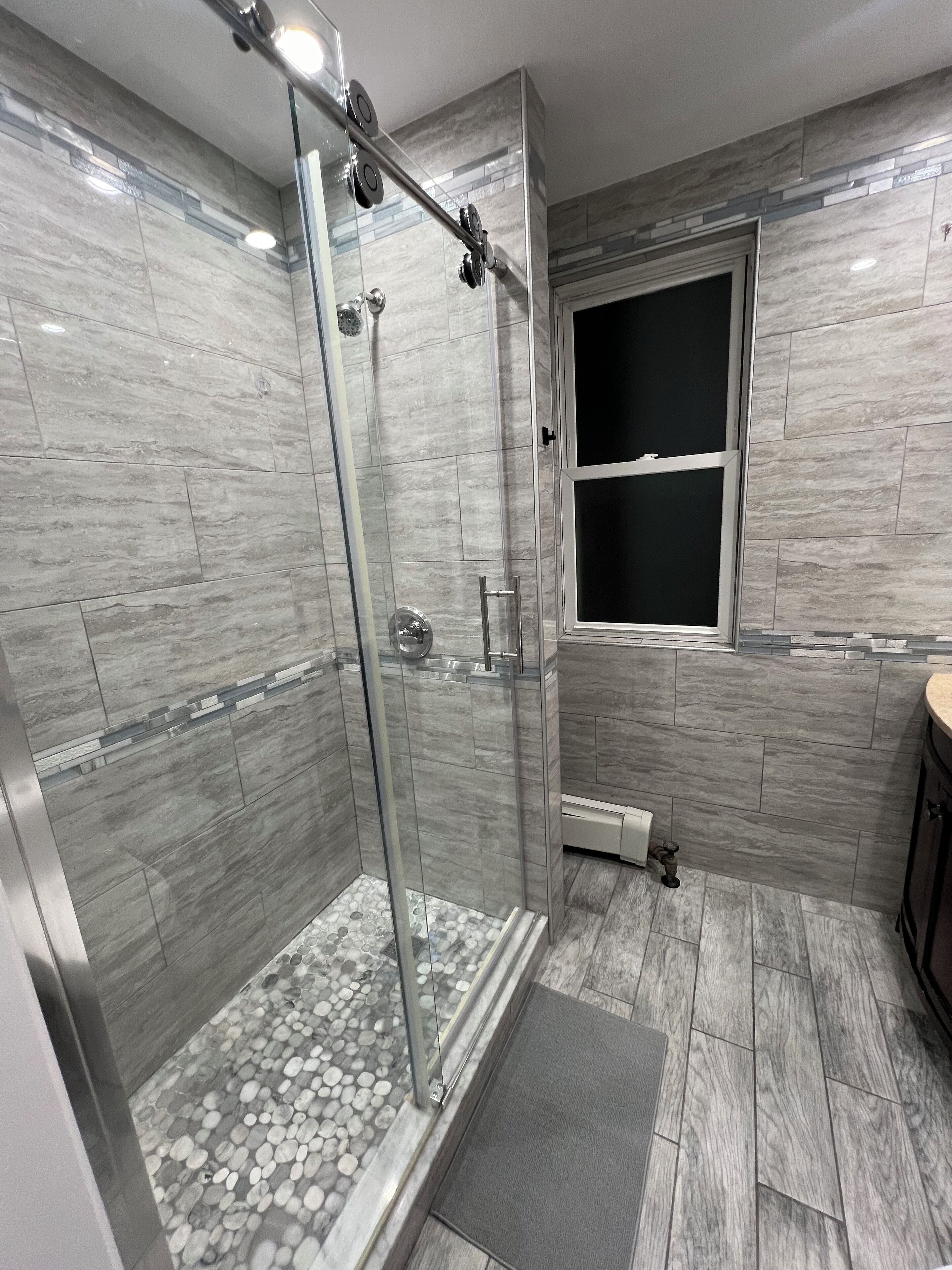 Un baño moderno con ducha de vidrio, azulejos de mármol y ventana integrada.