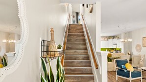 Eine Treppe mit Holzhinweisstufen und weißen Geländern, die zu einem Raum mit Küche und Essbereich führt.