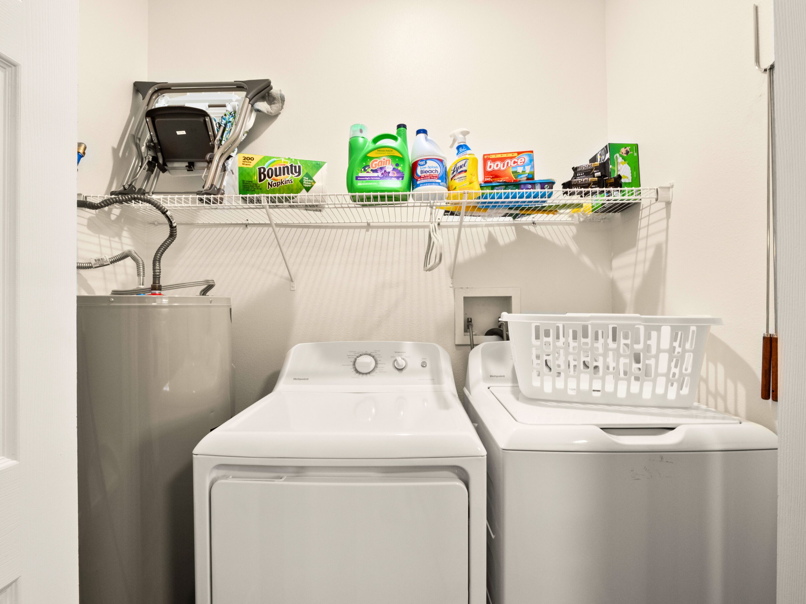 Een wasruimte met een wasmachine, droger en planken met wasmiddelen.