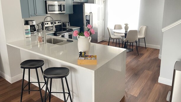 Une cuisine moderne avec des meubles bleus, un îlot central blanc et un coin repas avec des chaises blanches.