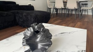 Un salon moderne avec une table basse en marbre, un canapé noir et un coin repas comprenant des chaises blanches et une table en verre.