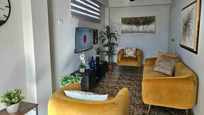 Sala de estar com ventilador de teto, televisão grande e dois poltronas amarelas.