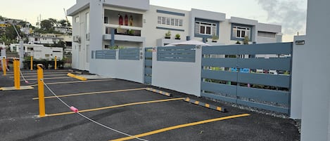 A parking lot with yellow bollards and a gated entrance to a building with balconies and potted plants.
