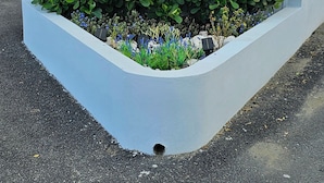 Placa para os Apartamentos Blue Breeze, com um logotipo de sol e onda, cercada por vegetação e estacionamento.