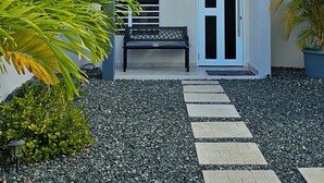 Um edifício moderno de dois andares com varanda, plantas em vasos e um caminho que leva à entrada.