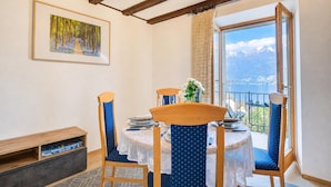 Ein Essbereich mit Tisch für zwei Personen, Holzstühlen, einem Bild an der Wand und Bergblick durch ein Fenster.