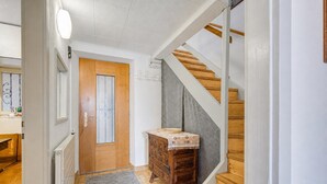 Ein Flur mit Holztür, einer Holztreppe und Stufen, einer kleinen Kommode und einem Heizkörper.
