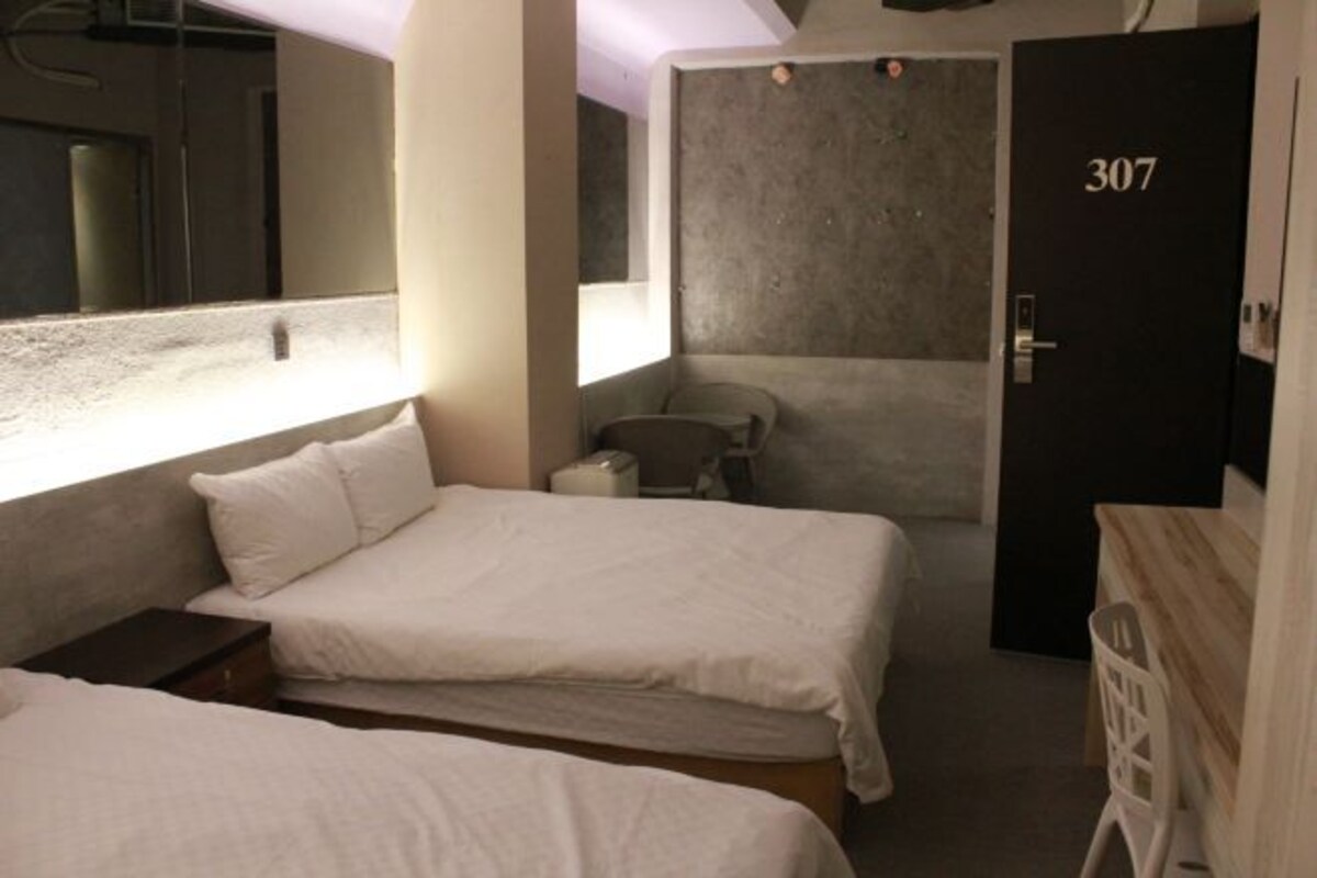Une petite chambre d’hôtel, de taille modeste, comprenant deux lits, une salle de bain et une porte portant le numéro 307.