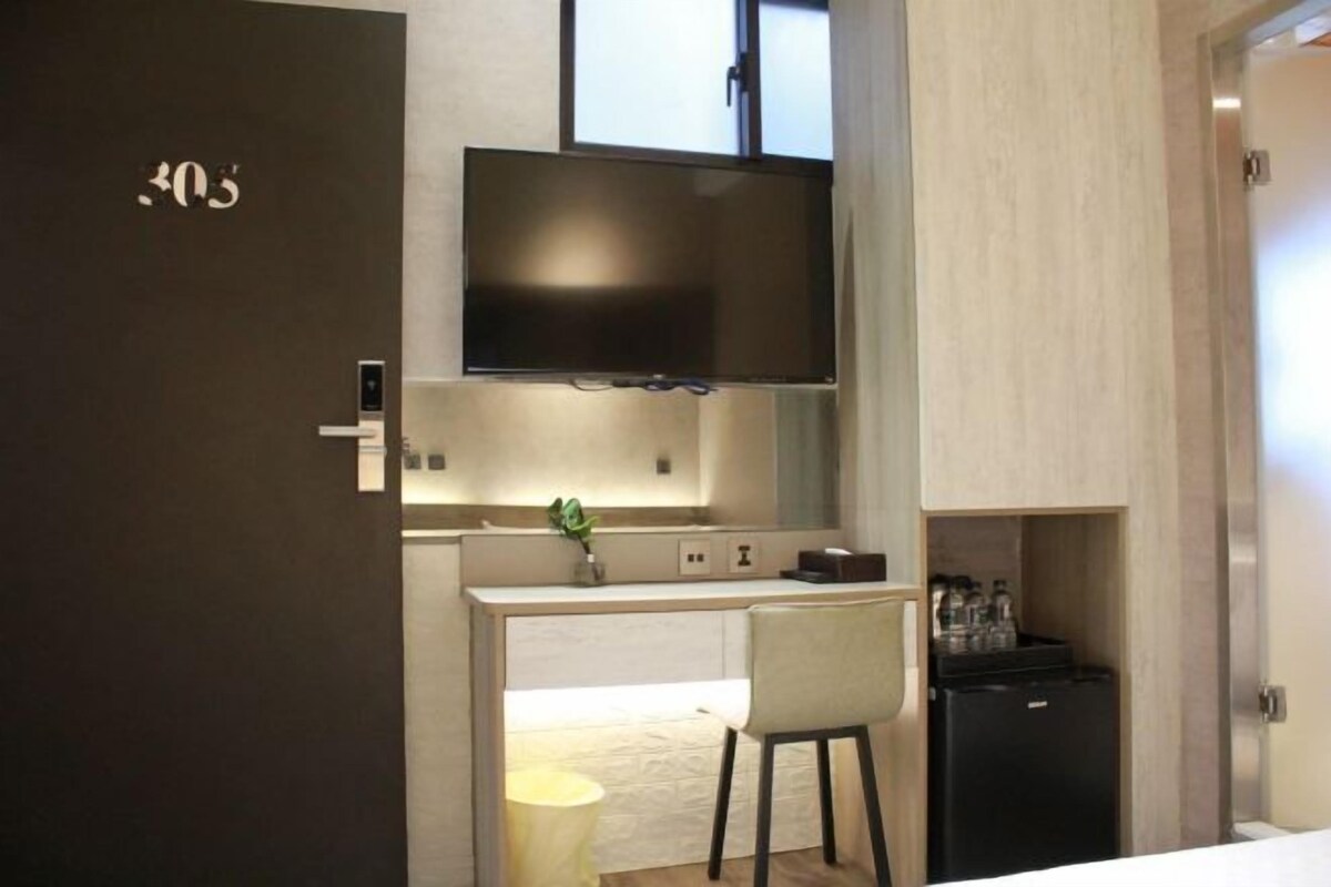 Une chambre d’hôtel moderne équipée d’un téléviseur à écran plat fixé au-dessus d’une petite kitchenette, d’un réfrigérateur compact et d’une seule chaise.