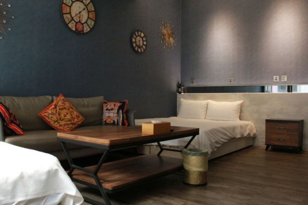 Une chambre moderne avec un lit, une table en bois, un canapé et une poubelle.