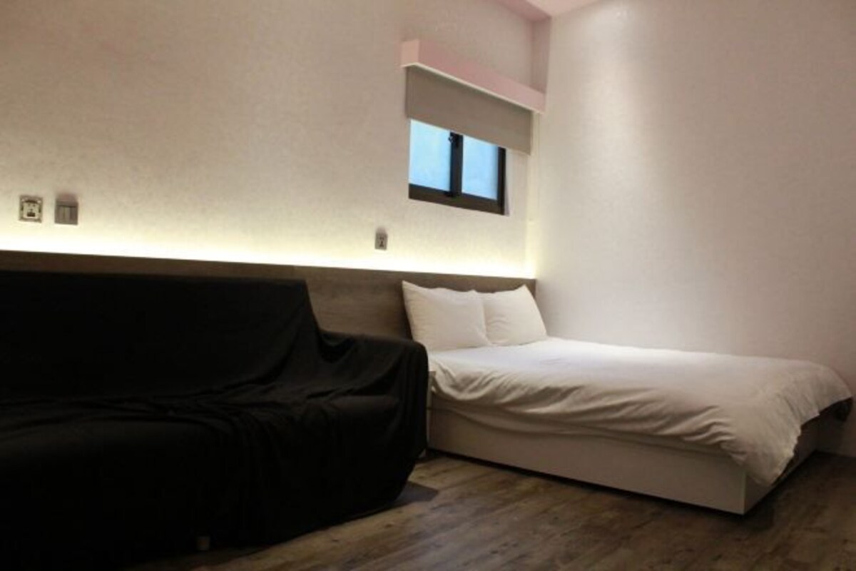 Une chambre à coucher avec un lit, un canapé noir et une petite fenêtre.