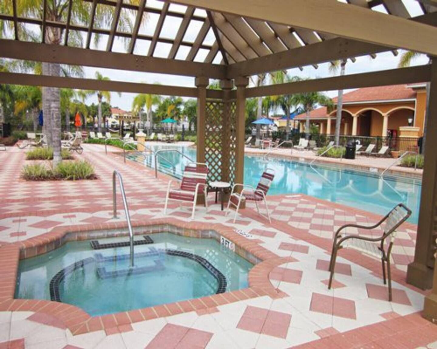 A pool area with a hot tub, lounge chairs, and a pergola structure.