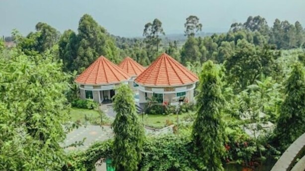A circular building with a red roof surrounded by lush greenery. - Ahaka cottages  (Mbarara)