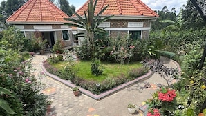 A garden with two buildings, a paved walkway, and various plants. - Ahaka cottages  (Mbarara)