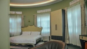 A hotel room with a bed, a desk, a chair, and curtains. - Ahaka cottages  (Mbarara)