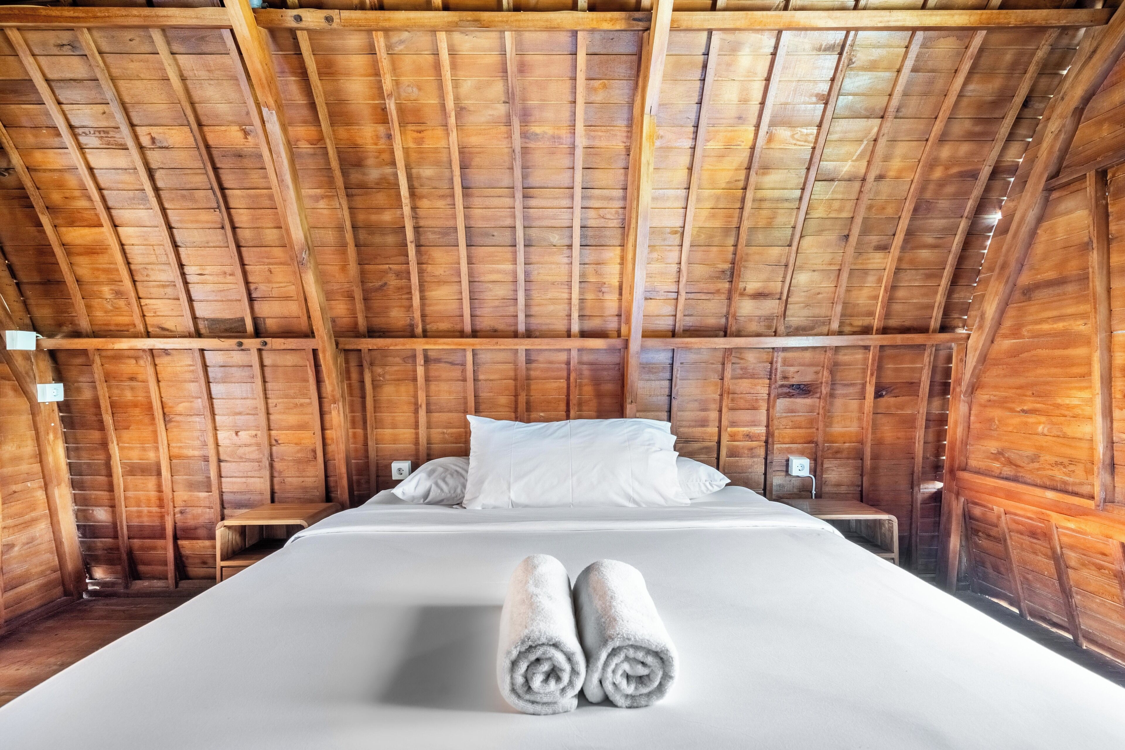 Une chambre mansardée en bois, avec un lit, des oreillers et des serviettes enroulées.