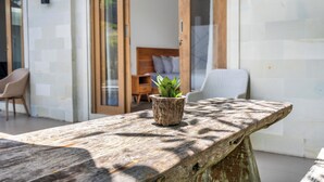 Una mesa de madera con una planta en maceta, un banco de madera y una cama con almohadas al fondo.