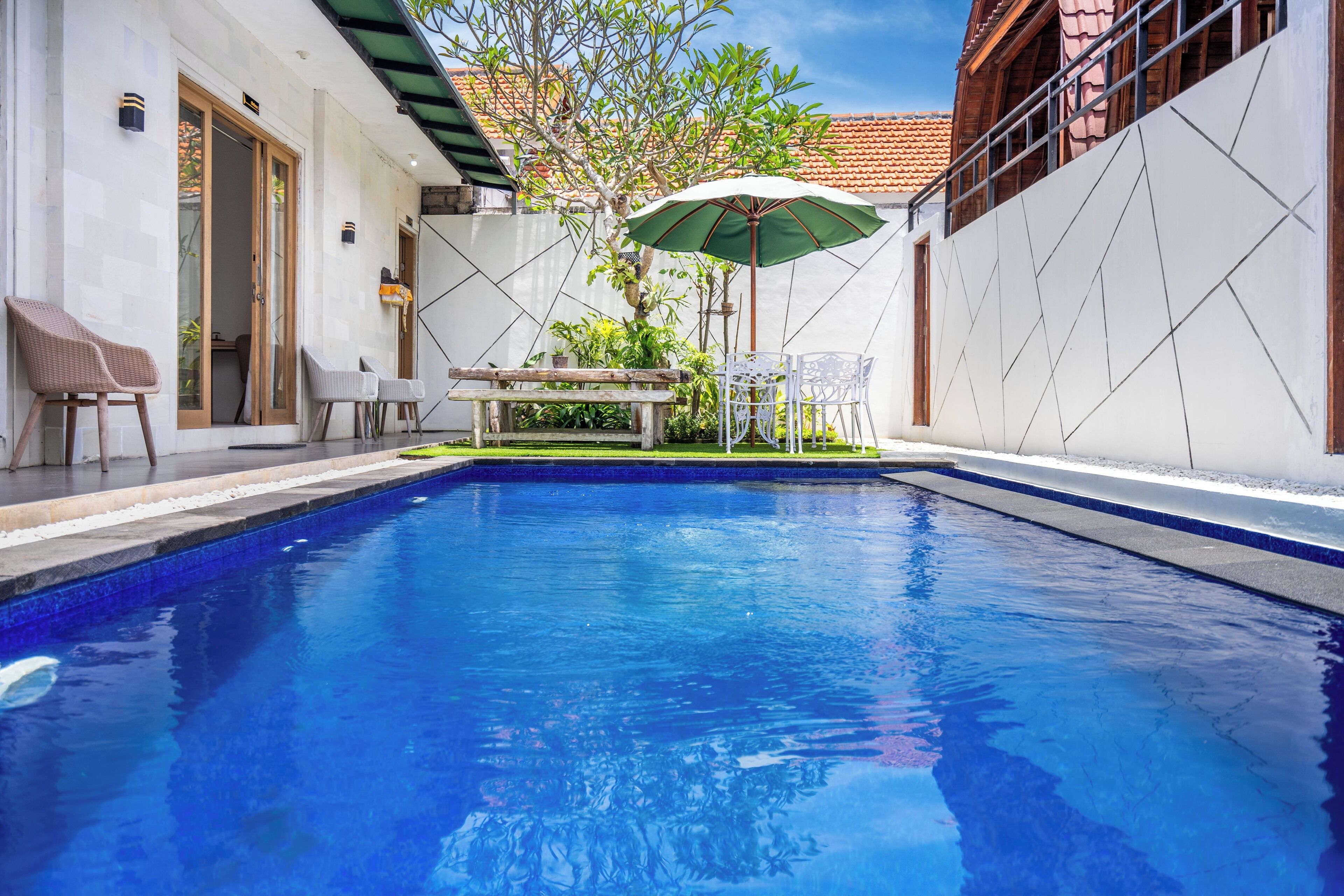 A swimming pool with a wooden deck, outdoor seating, and a green umbrella.