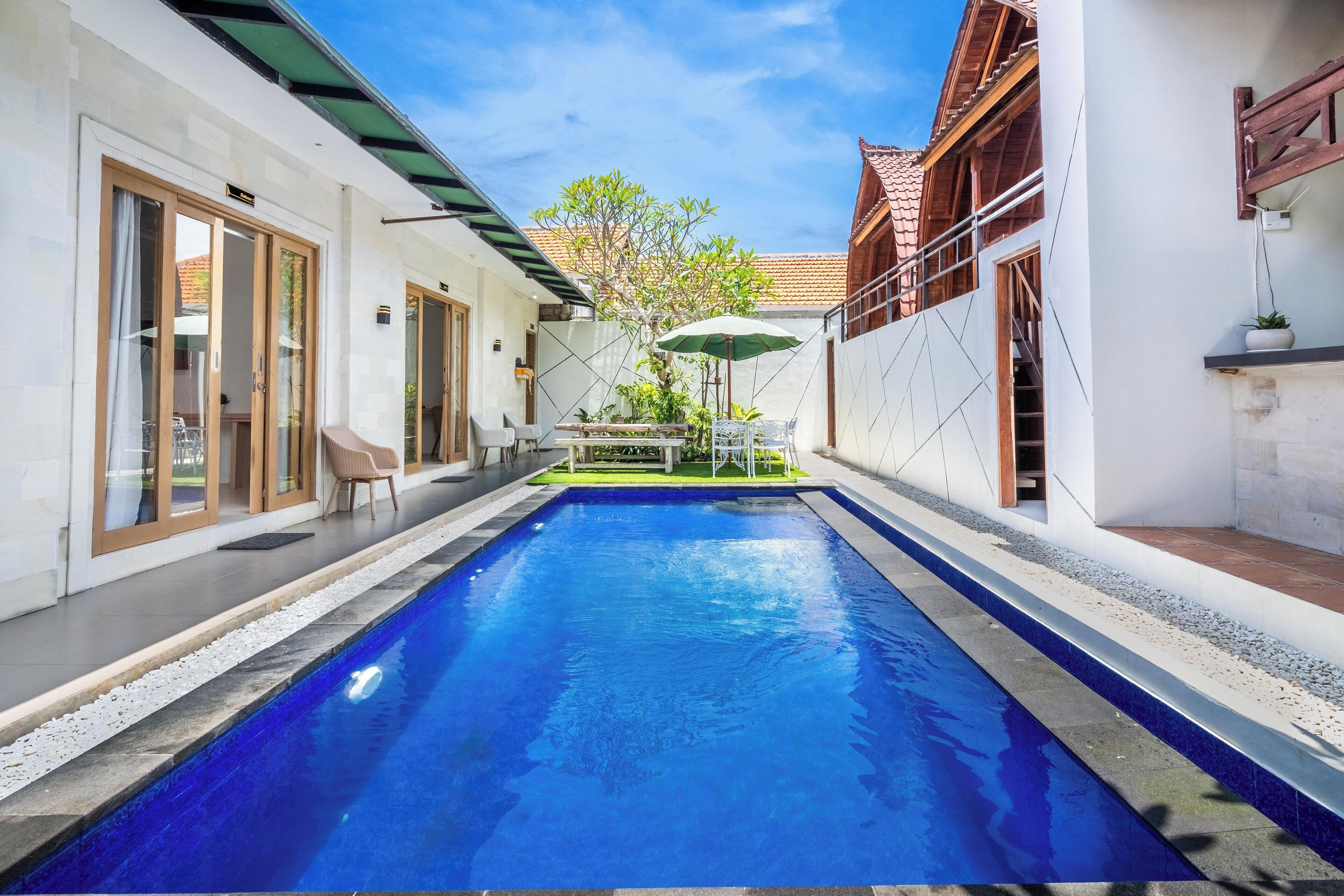 Une piscine à l’eau d’un bleu cristallin, entourée d’un bâtiment blanc doté d’un toit en tuiles et d’une structure en bois en arrière-plan.