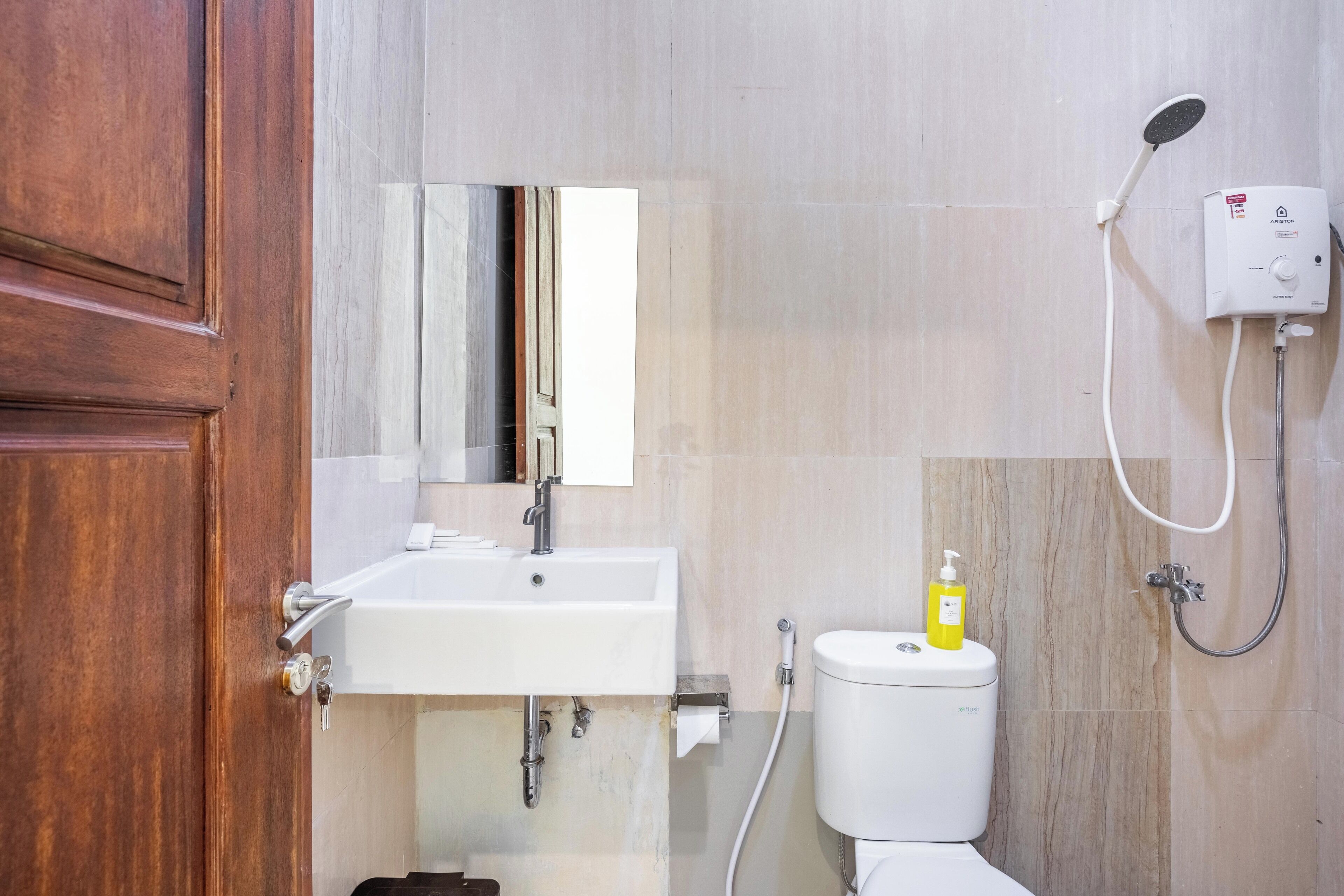 A bathroom with a wooden door, a white sink, a toilet, and a shower unit.
