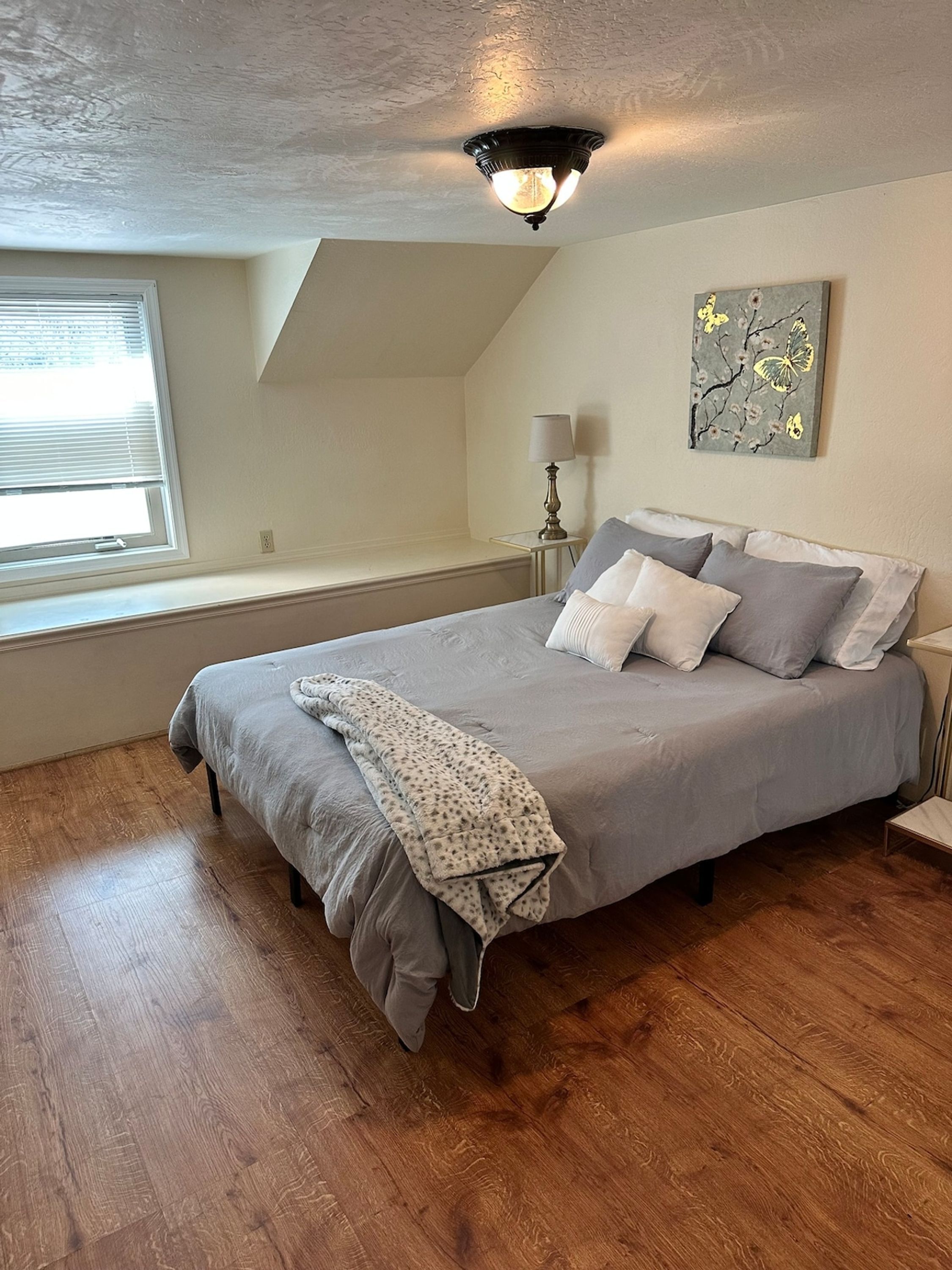 A bedroom with a bed, a window, a lamp, and a painting on the wall.