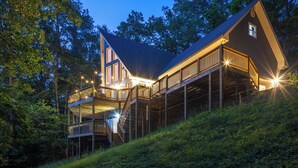 A multi-level wooden cabin with outdoor decks and stairs, surrounded by trees.