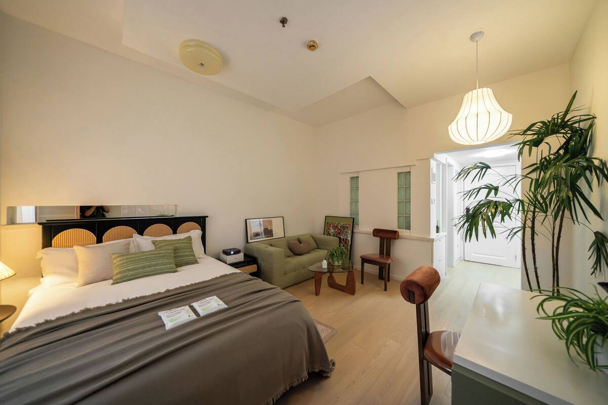 Ein modernes Schlafzimmer mit Bett, Nachttisch, grünem Sofa und einer Essecke mit Stuhl und Tisch.