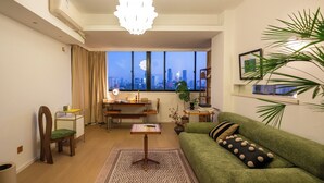 Un salón moderno con un sofá verde, un escritorio y vistas de la ciudad a través de amplias ventanas.