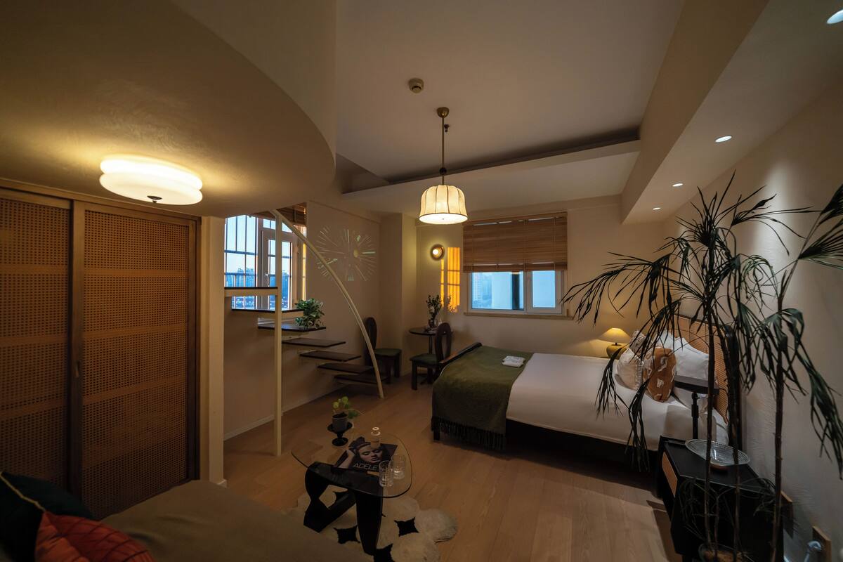 Ein modernes Hotelzimmer mit einem Bett, einem Schreibtisch, einem Stuhl und einer großen Pflanze.