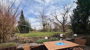 Un patio al aire libre con una mesa y sillas de madera, rodeado de un jardín con diversas plantas y árboles.
