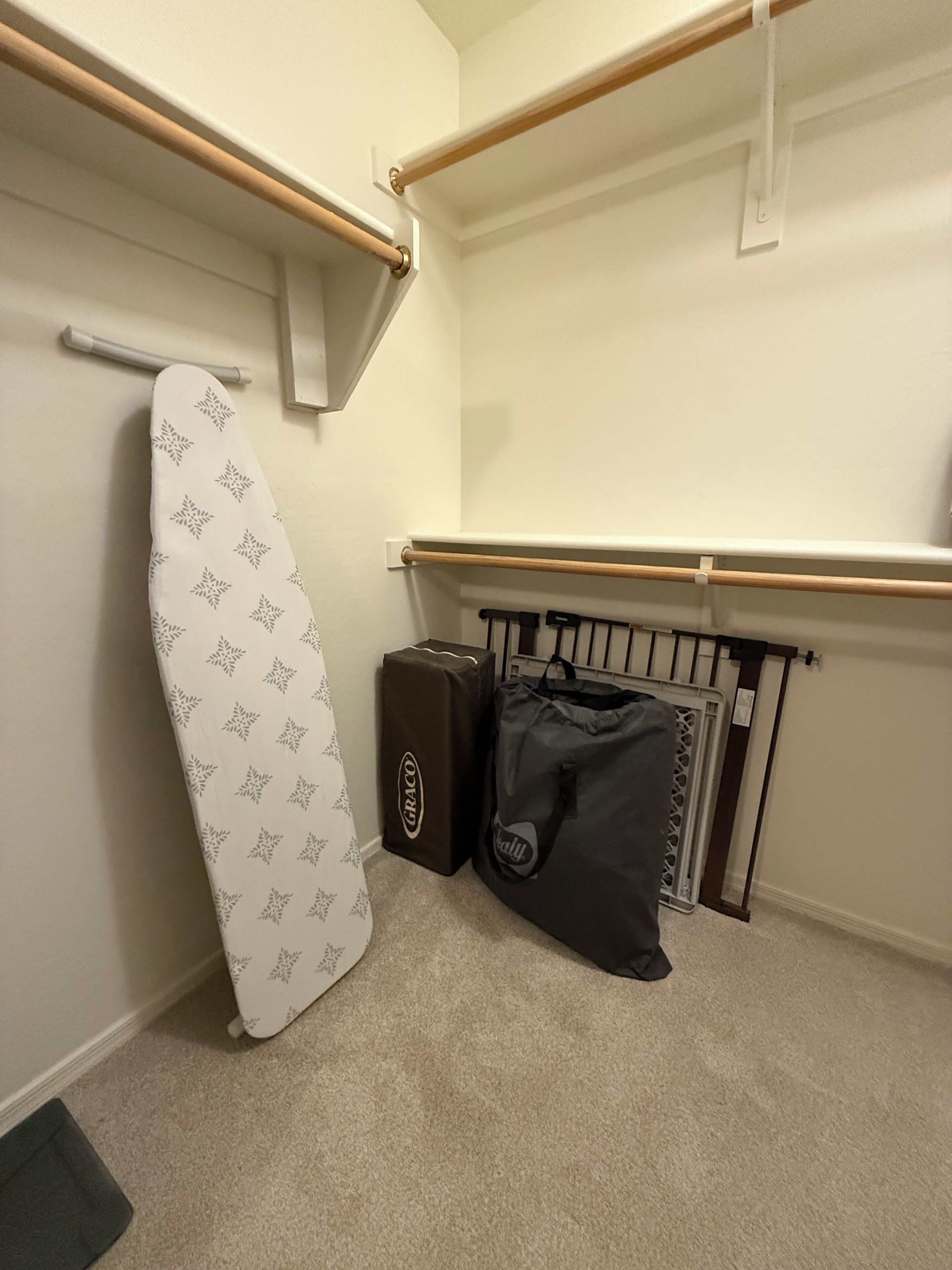 A corner of a room with a white iron, a black Graco bag, and a black bag with a gray tag.