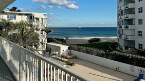 Ein Balkon mit Blick auf Strand und Meer, ein Schwimmbecken und ein Hochhaus.