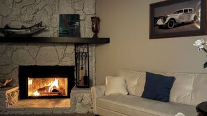 A living room with a stone fireplace, a white sofa with blue cushions, and a framed picture of a car on the wall.
