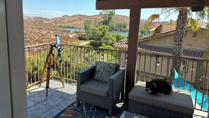 A balcony with a view of a lake, a chair, a small table, and a telescope.