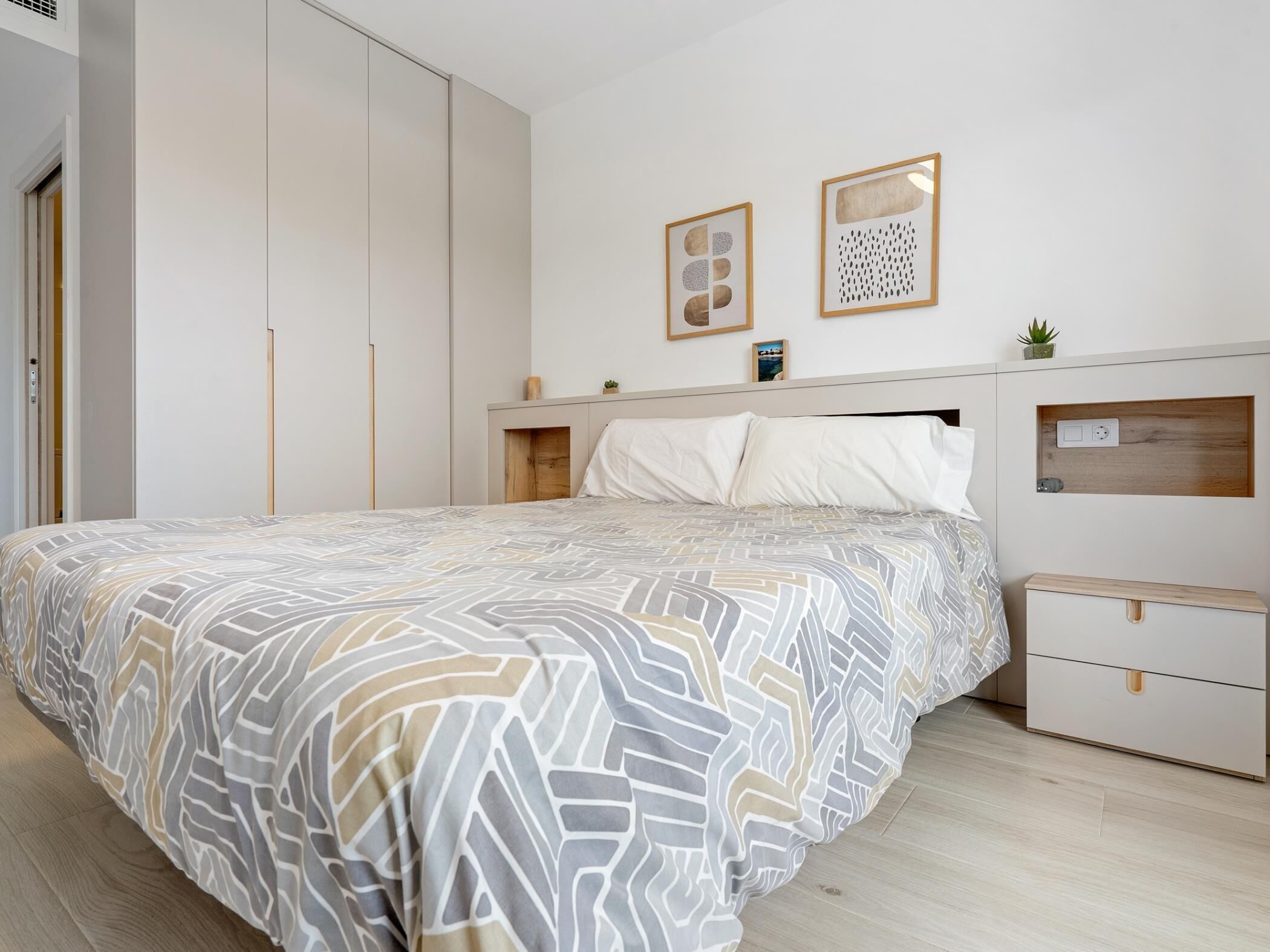 Un dormitorio con cama, armario, mesita de noche y dos marcos con cuadros en la pared.