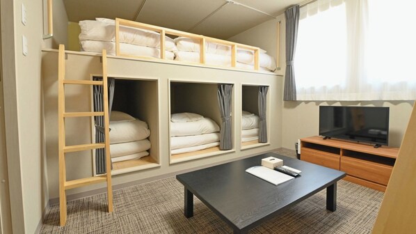 A compact hotel room with a bunk bed, a TV, a desk, and a small seating area.