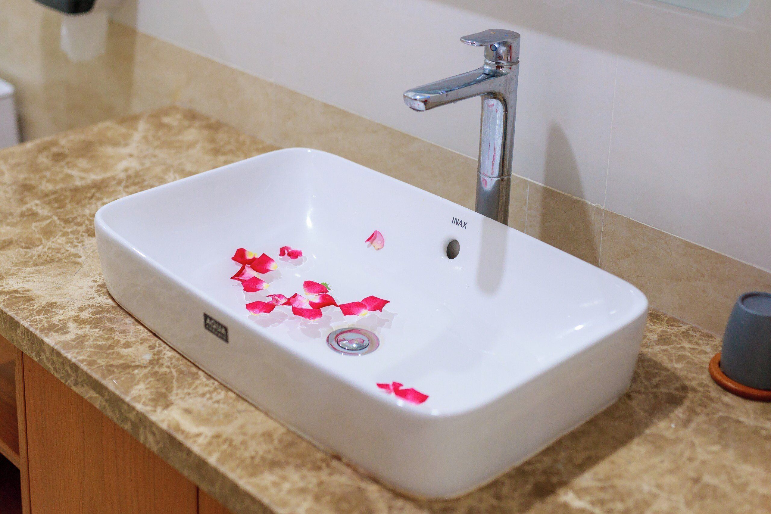 A white bathroom sink with a single faucet, a beige countertop, and a small trash bin to the right.