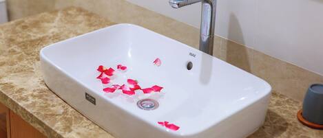 A white bathroom sink with a single faucet, a beige countertop, and a small trash bin to the right.