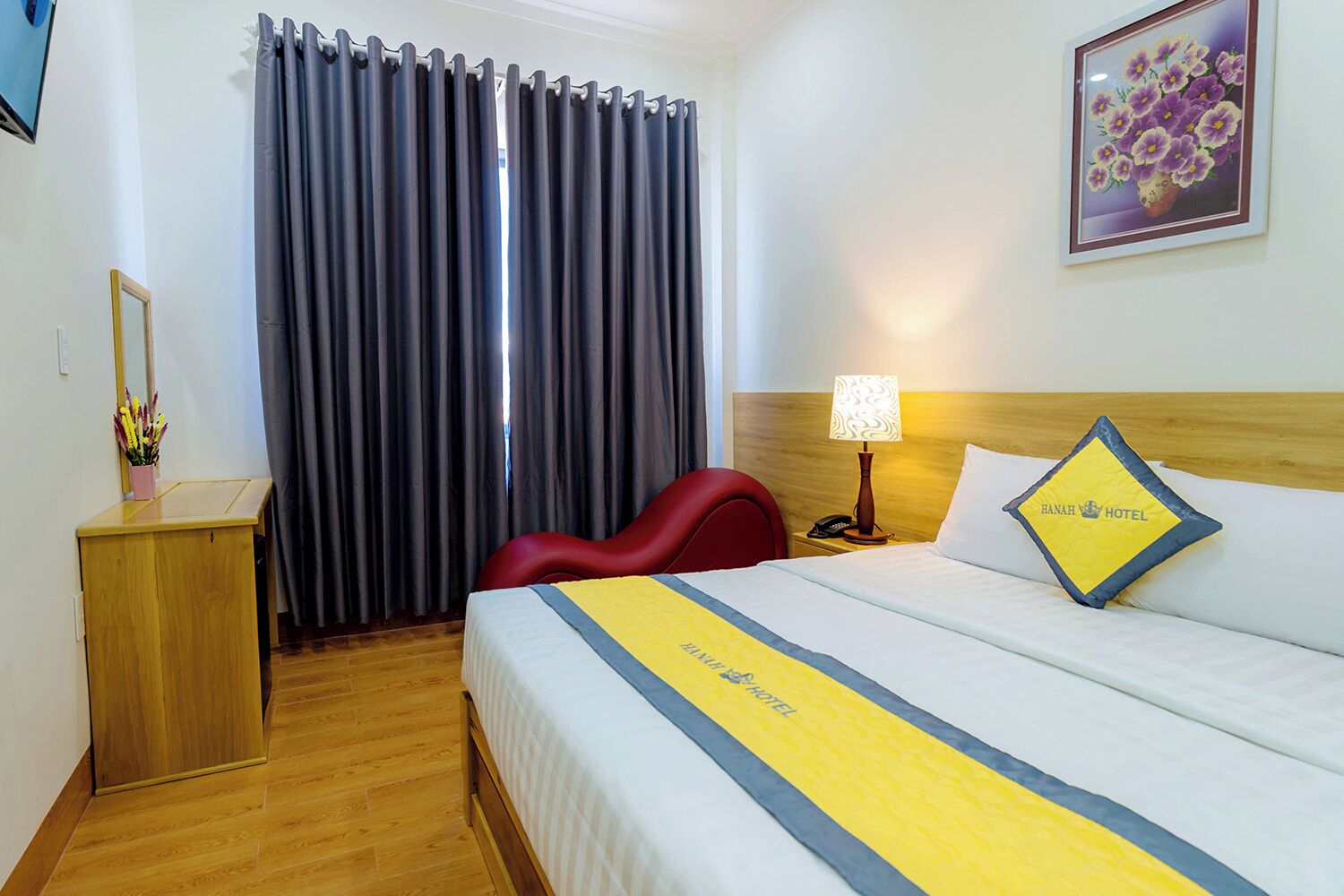 A hotel room with a bed, a desk, a chair, a lamp, and a painting on the wall.