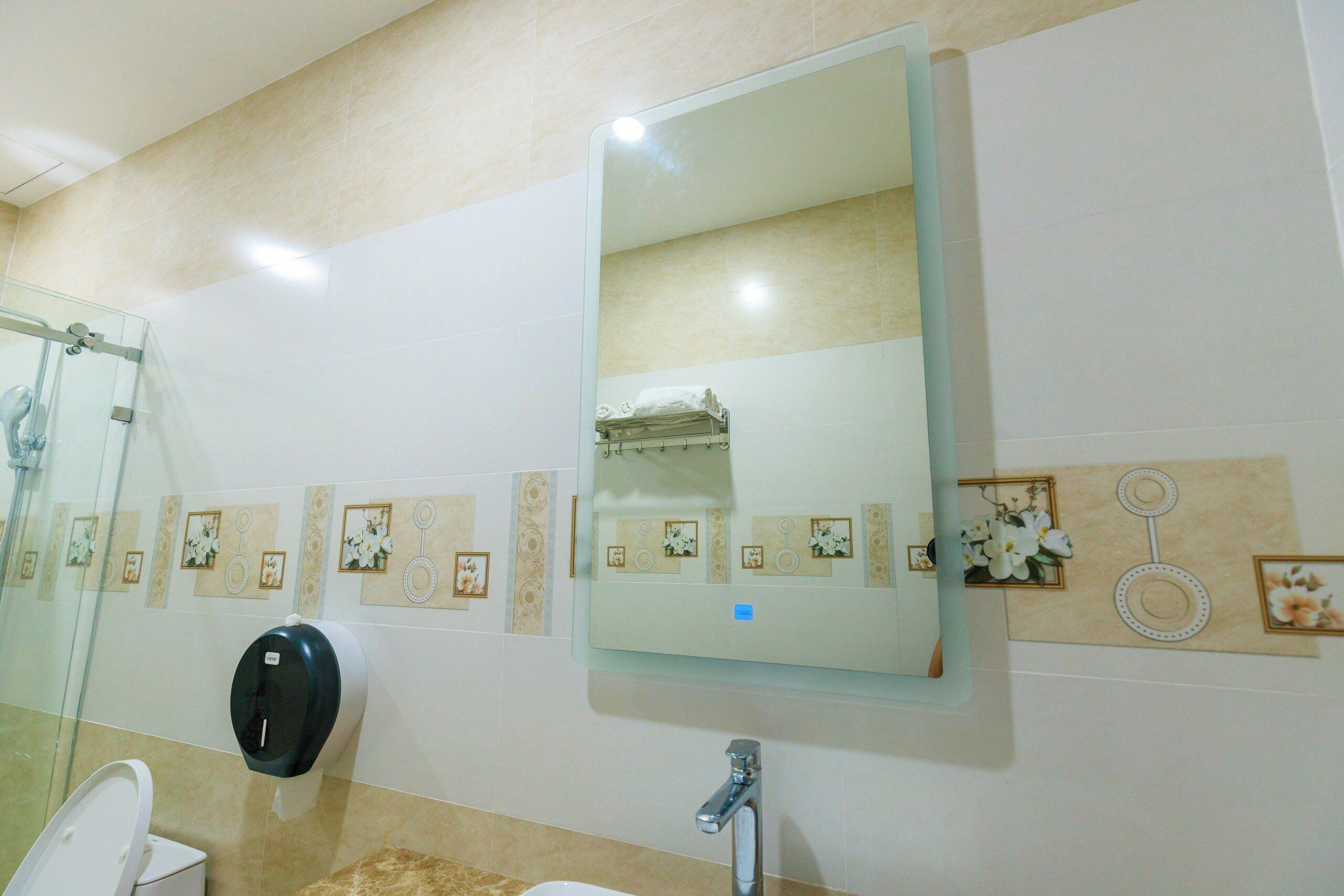 Un baño con cabina de ducha de vidrio, inodoro, lavabo con espejo y azulejos decorativos.