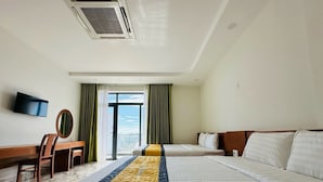 Habitación de hotel con dos camas, un escritorio con silla, televisor montado en la pared y un gran ventanal con cortinas.
