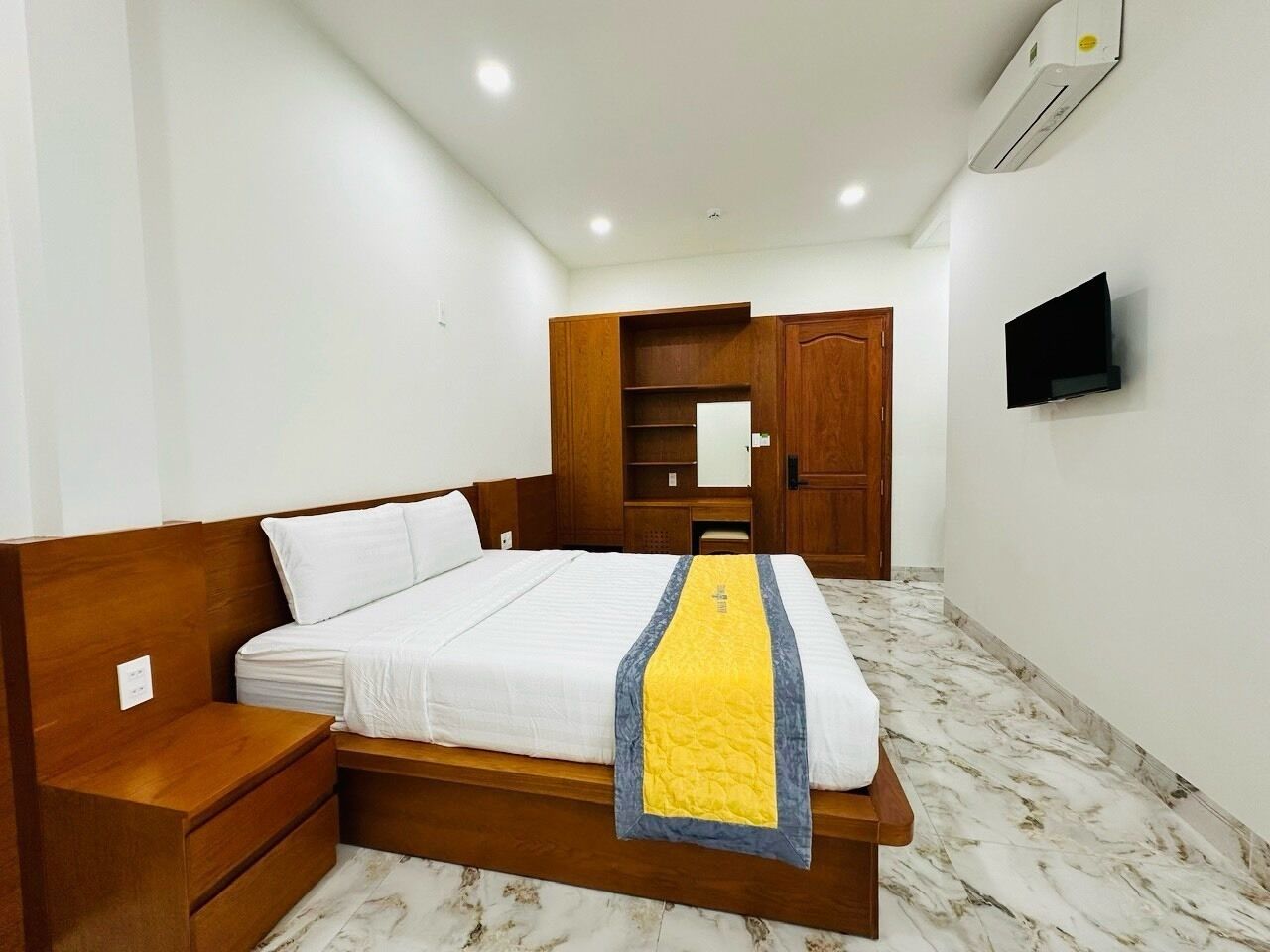 A neatly arranged bedroom with a bed, bedside tables, a wardrobe, a TV, and an air conditioning unit.