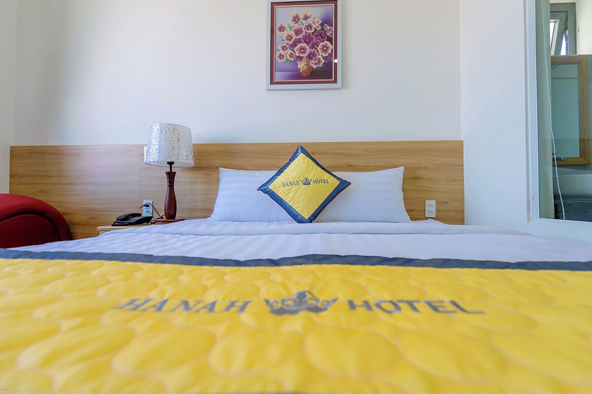Habitación de hotel con cama, mesita de noche, lámpara y almohada con el logotipo del hotel.