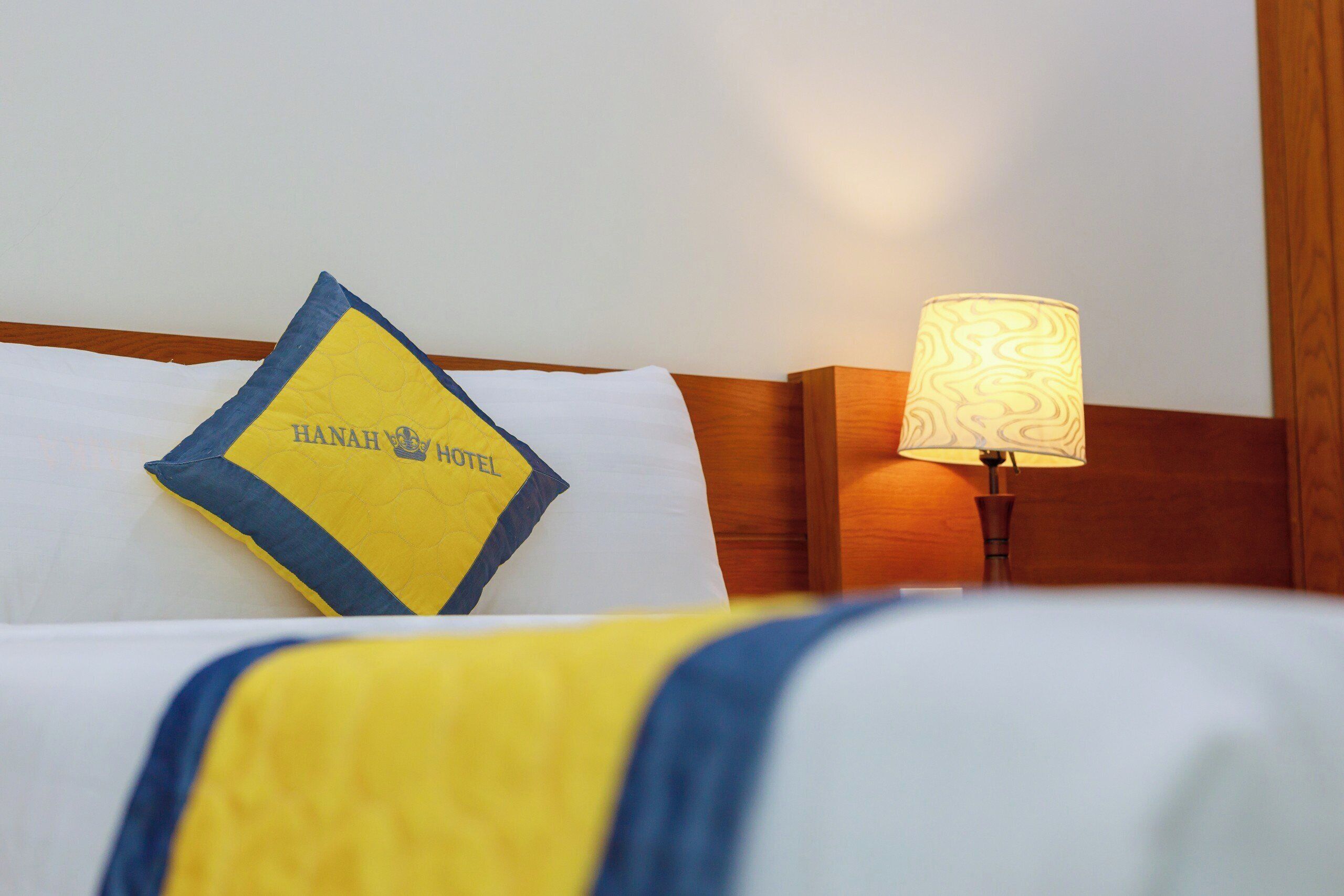 Una habitación de hotel con una cama, una almohada con el nombre del hotel y una lámpara.