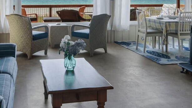 Un vaste espace intérieur avec vue sur l’océan, doté d’un plafond en bois, d’un ventilateur de plafond et d’un coin repas avec des chaises et une table.