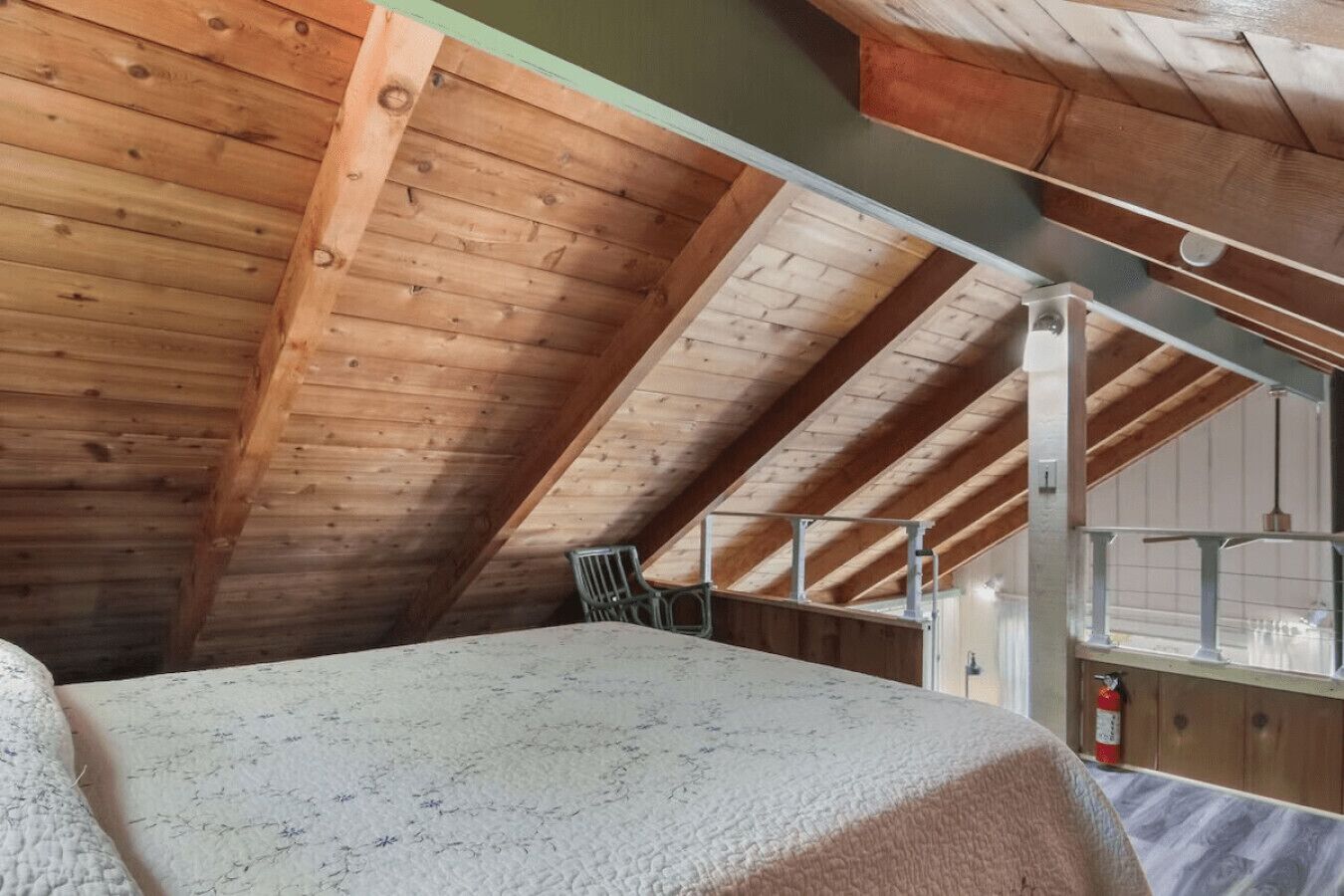 A high-ceilinged attic bedroom with exposed wooden beams, a bunk bed, and a small chair.